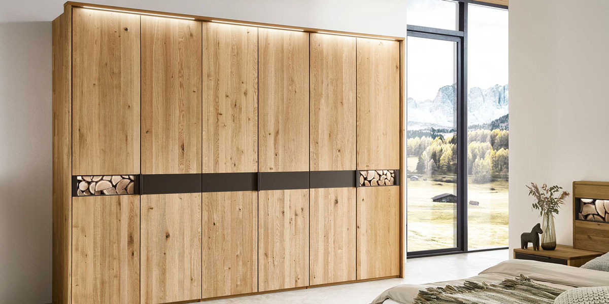 Wöstmann Kleiderschrank Banner zeigt 6-türigen Kleiderschrank in eine stilvolle und funktionale Wohlfühloase, in Wildeiche und Spaltholz Akzent.