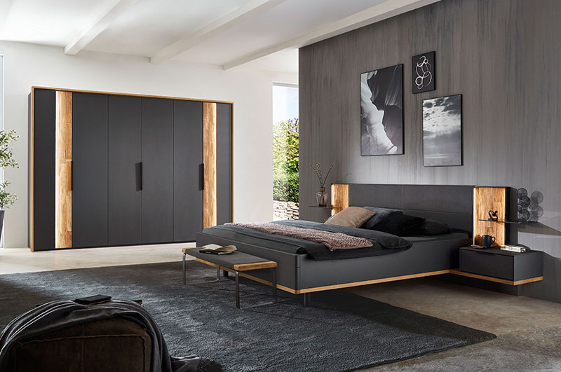 Schlafzimmer WSL 8800  Hier werden Sie zu der Schlafzimmer Serie WSL 8800 weitergeleitet: Kachel zeigt ein Schlafzimmer, Doppelbett, zwei Konsolen und 6 türigen Kleiderschrank in graphitgrauen Lack Fronten mit zwei seitlichen senkrecht angeordneten Spaltholz Akzenten.