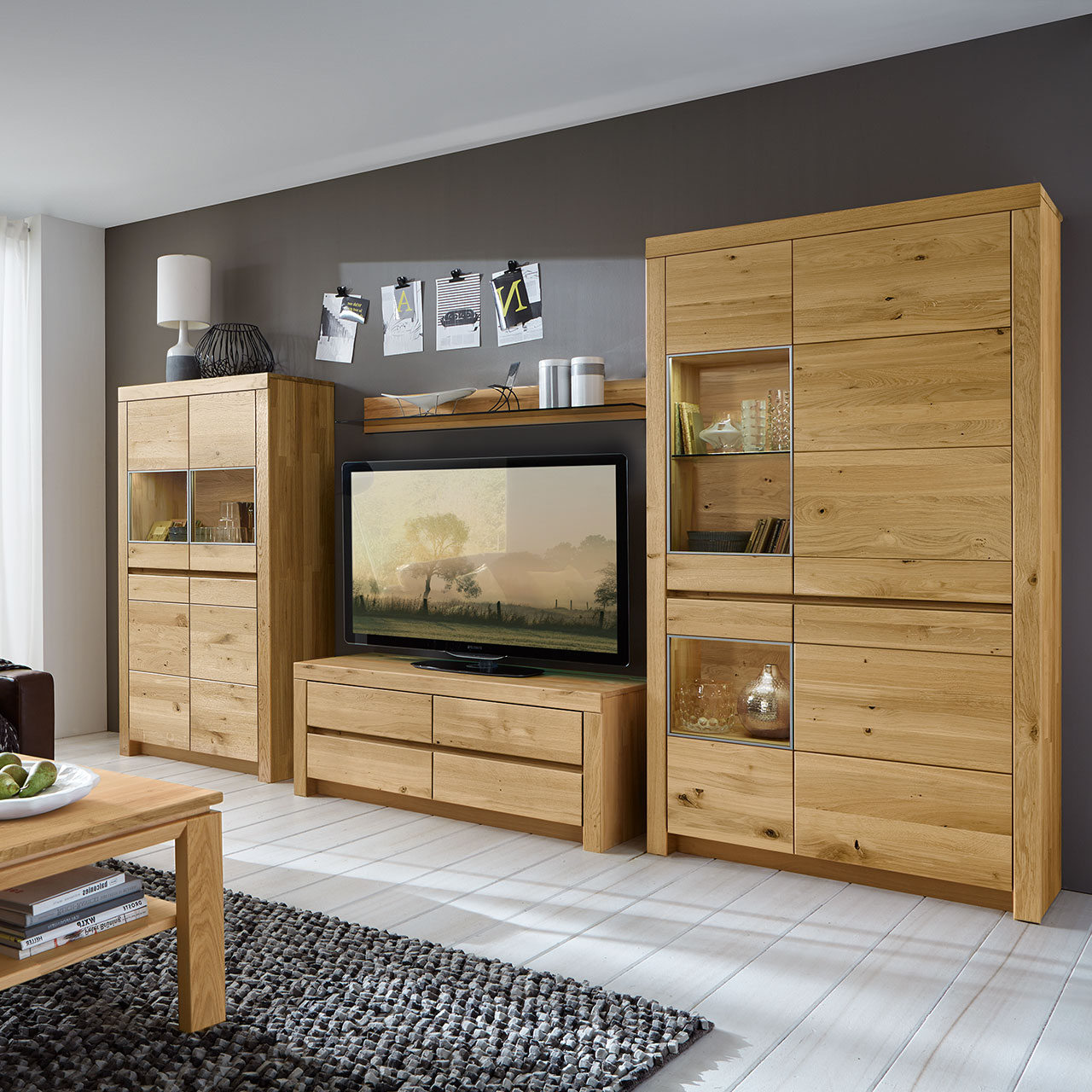 Wohnwand in massiver Wildeiche Type 3106 mit ein Lowboard, ein Zeilenschrank und einem Highboard bestehend aus 4 Türen mit zwei Vitrinenfächern nebeneinander angeordnet, als Ambiente Bild.